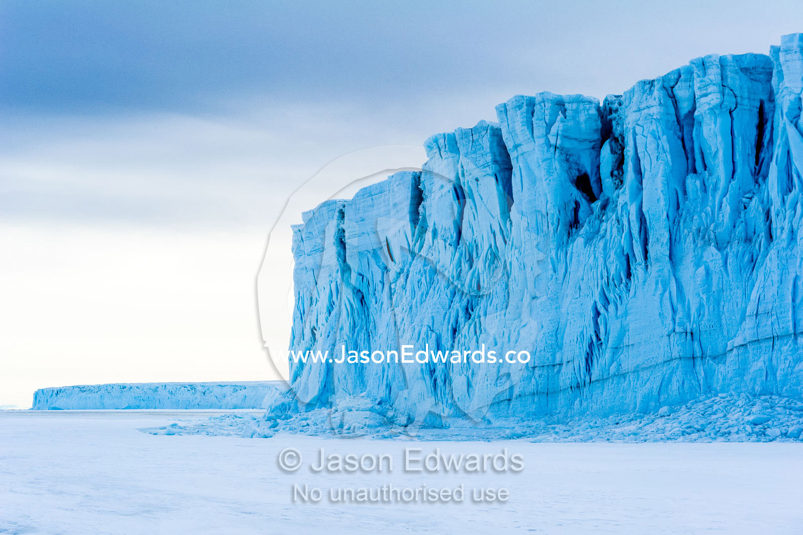 The sheer impregnable ice cliffs of a glacier tower over the frozen sea ice. Barne Glacier, Ross Sea, Ross Island, Antarctica.