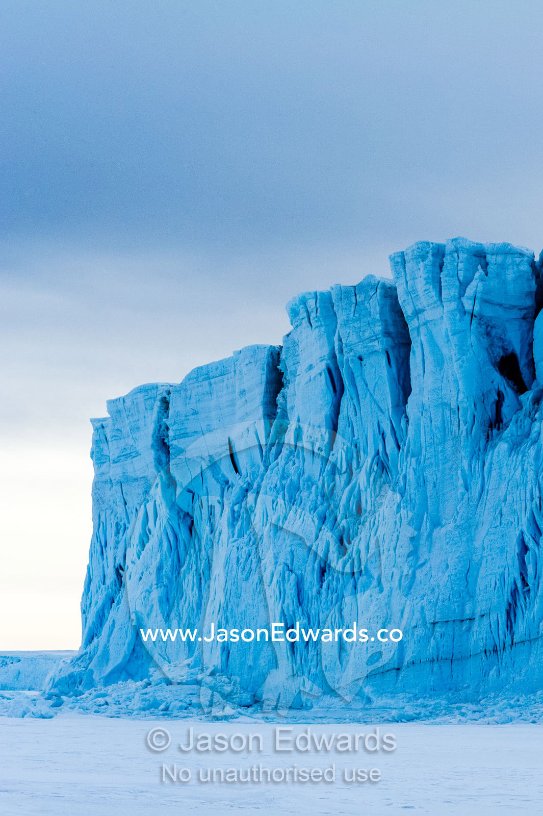 The sheer impregnable ice cliffs of a glacier tower over the frozen sea ice. Barne Glacier, Ross Sea, Ross Island, Antarctica.