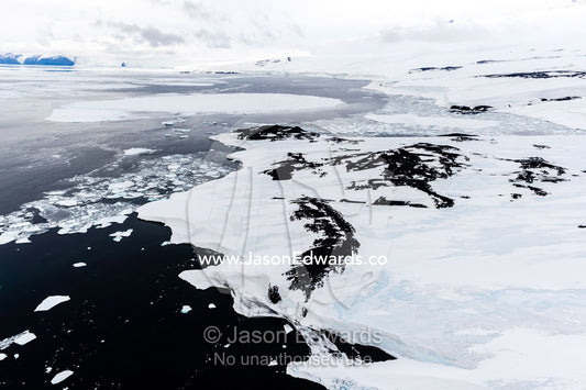 Melting sea ice, icebergs and ice cliffs along a rugged and inhospitable bay in Antarctica. Maumee Bight, Wohlschlag Bay, Ross Island, Antarctica.