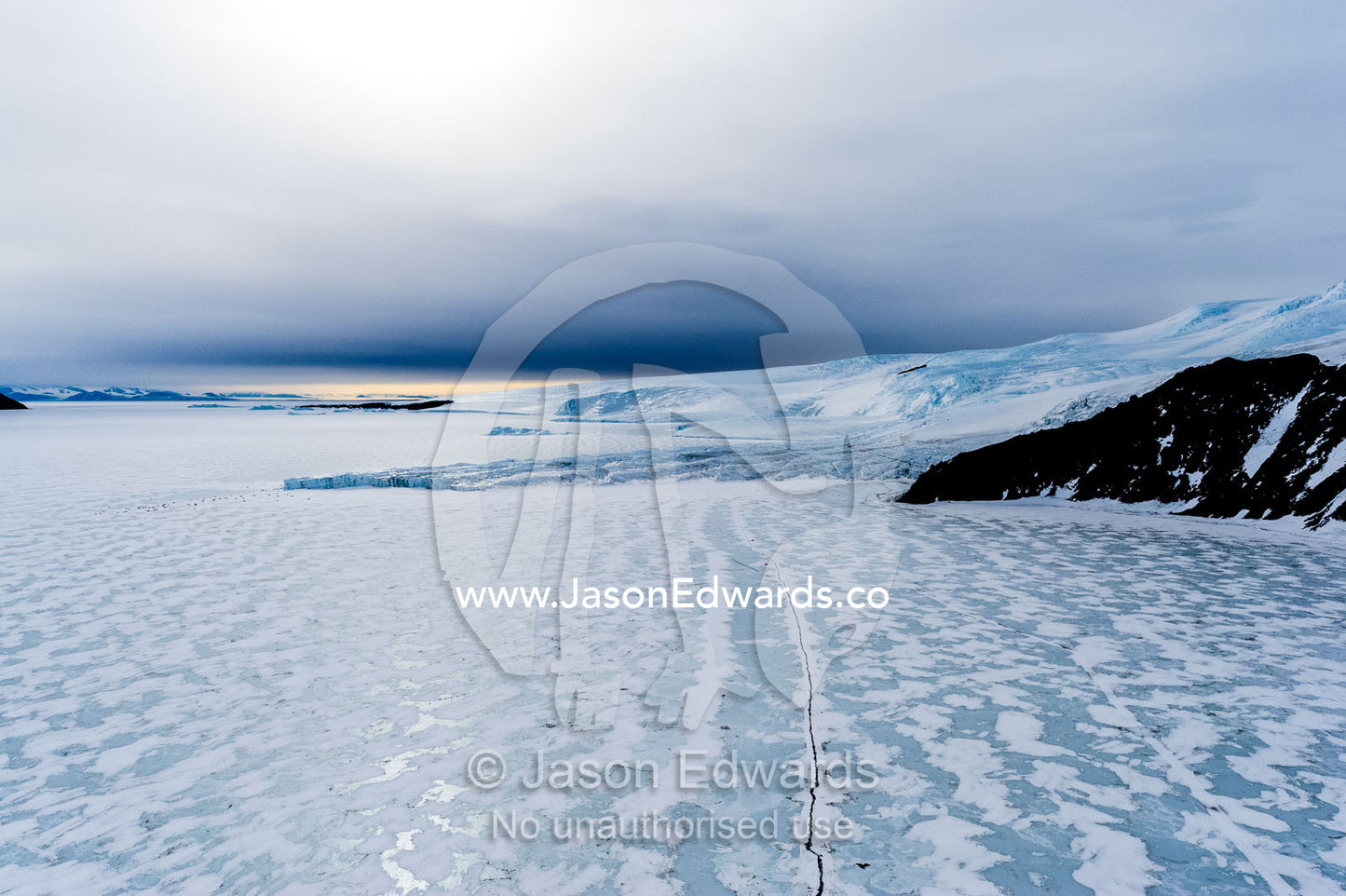 The sheer impregnable ice cliffs of a glacier tower over the frozen polished sea ice. Lands End, Tryggve Point, McMurdo Sound, Ross Island, Antarctica.
