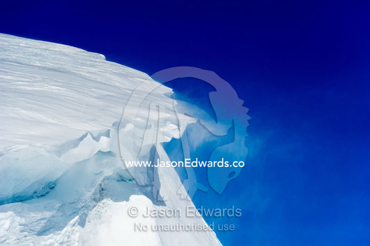 Strong winds blow snow and ice from a cliff overhang. Hutton Cliffs, Erebus Bay, McMurdo Sound, Ross Island, Antarctica.