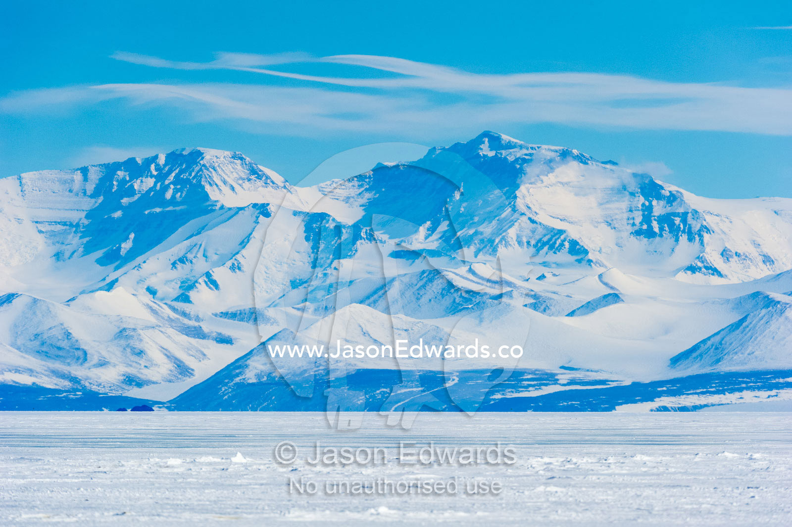An enormous mountain range rises above the flat plain of sea ice. Royal Society Range, Haskell Strait, McMurdo Sound, Ross Island, Antarctica.