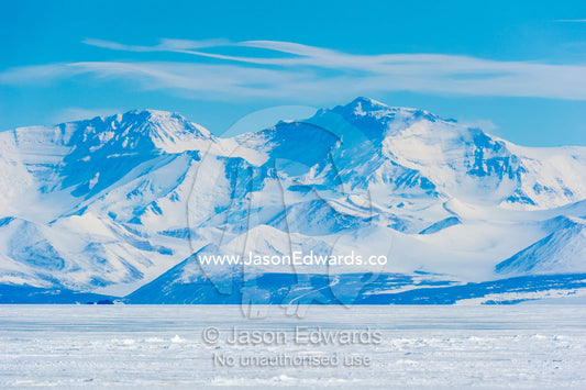 An enormous mountain range rises above the flat plain of sea ice. Royal Society Range, Haskell Strait, McMurdo Sound, Ross Island, Antarctica.