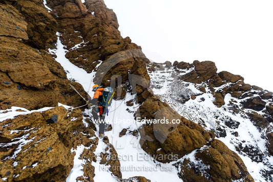 Mountain climbers using climbing ropes to scale a cliff overlooking the Ross Ice Shelf. Castle Rock, Hut Point Peninsula, Ross Island, Antarctica.