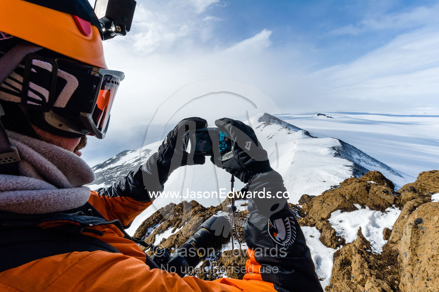 A mountain climber uses a pocket camera to photograph Mount Erebus an active volcano from a mountaintop. Breached Cone, Castle Rock, Hut Point Peninsula, Ross Island, Antarctica.