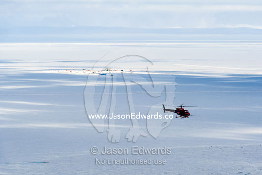 A helicopter flies over the frozen sea ice in Antarctica. Royal Society Range, Pegasus Field, McMurdo Ice Shelf, Ross Island, McMurdo Sound, Antarctica.