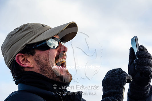 A man laughs whilst taking a selfie on a cell phone in Antarctica. Observation Hill, McMurdo Station, Ross Island, Antarctica.