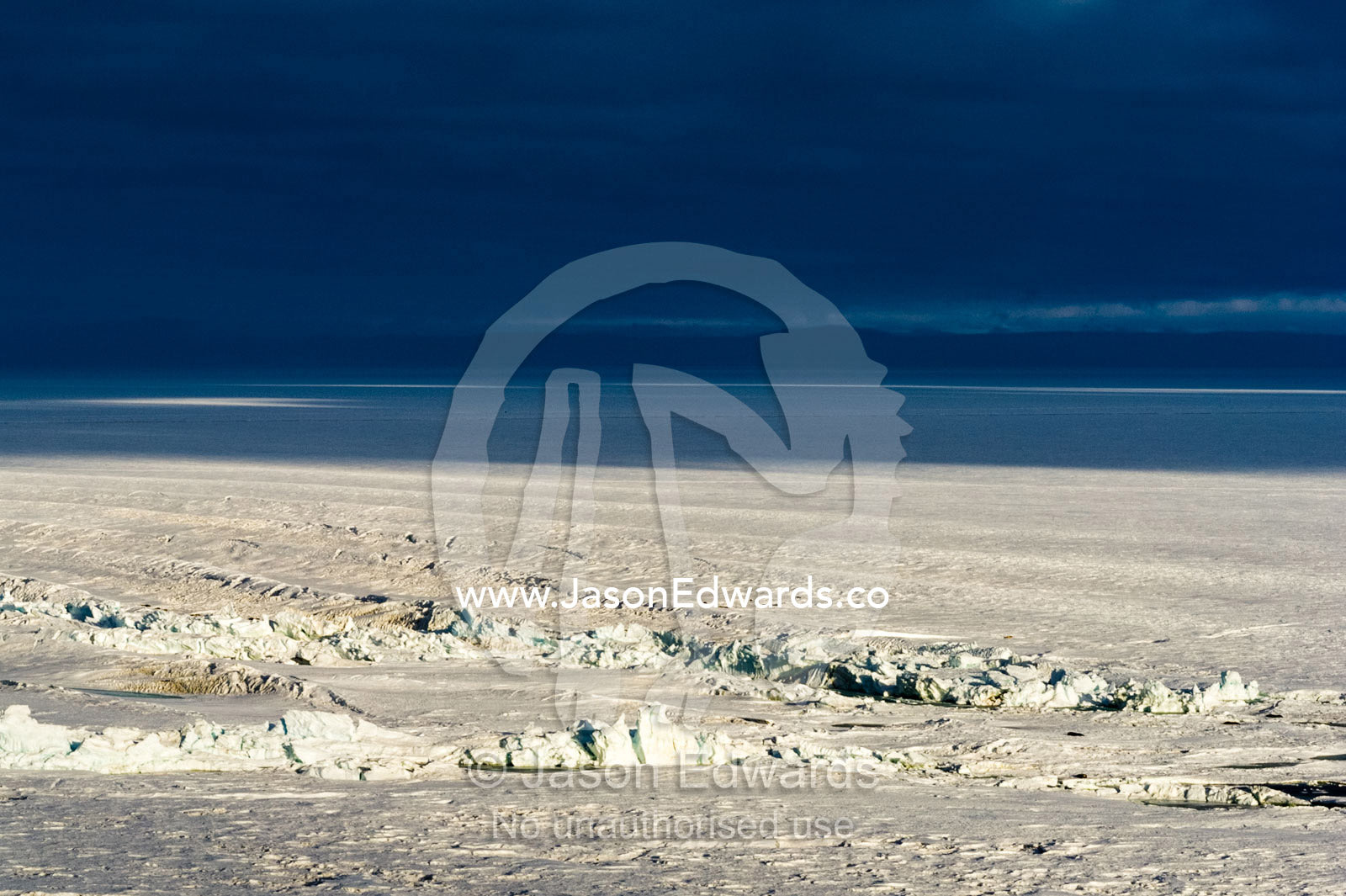 A sunray pierces a dark storm cloud illuminating jagged pressure ridges in the sea ice. Pram Point, McMurdo Sound, Ross Island, Antarctica.