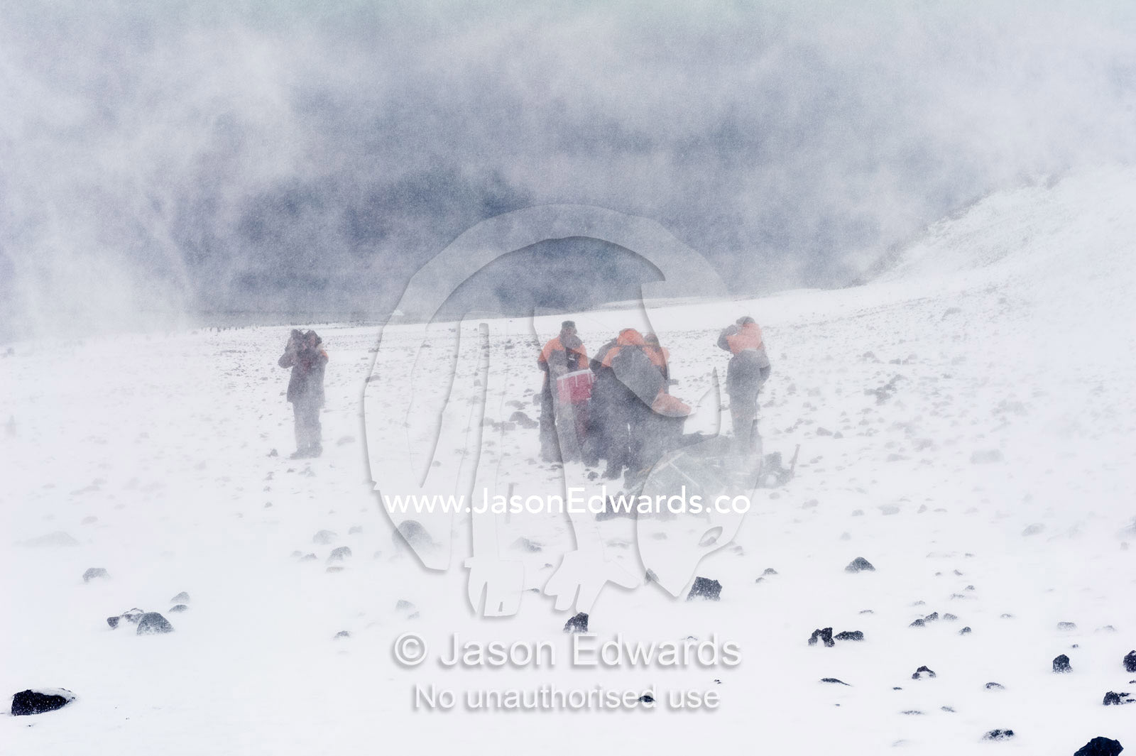 Researchers stand in a cloud of snow from a helicopter on a beach in Antarctica. Caughley Beach, Cape Bird, Ross Island, Antarctica.