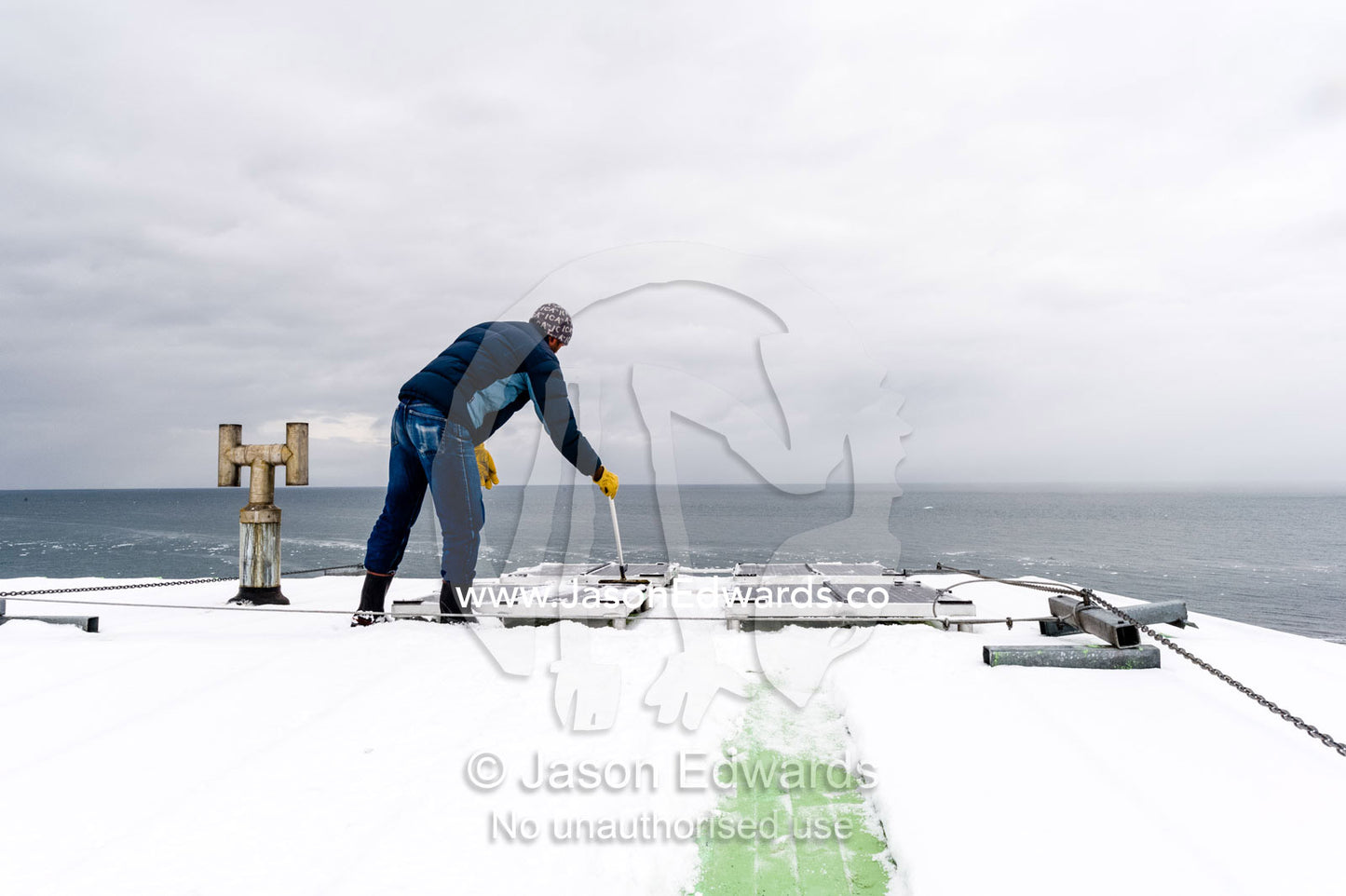 A volunteer sweeps snow form the solar panels of a remote Adelie Penguin research station in Antarctica. Cape Bird, Ross Island, Antarctica.
