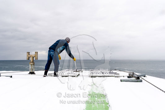 A volunteer sweeps snow form the solar panels of a remote Adelie Penguin research station in Antarctica. Cape Bird, Ross Island, Antarctica.