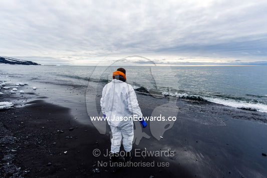 A researcher wearing a safety suit washes his tools in the ocean after collecting samples from a dead Weddell Seal. Caughley Beach, Cape Bird, Ross Island, Antarctica.