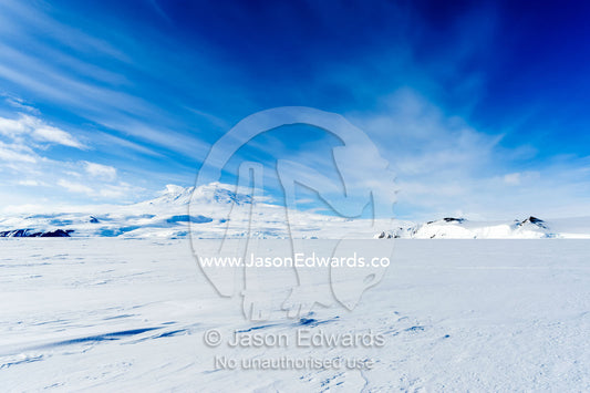 Drifts of snow blow across the barren sea ice beneath Mount Erebus an active volcano. Turtle Rock, Erebus Bay, McMurdo Sound, Ross Island, Antarctica.