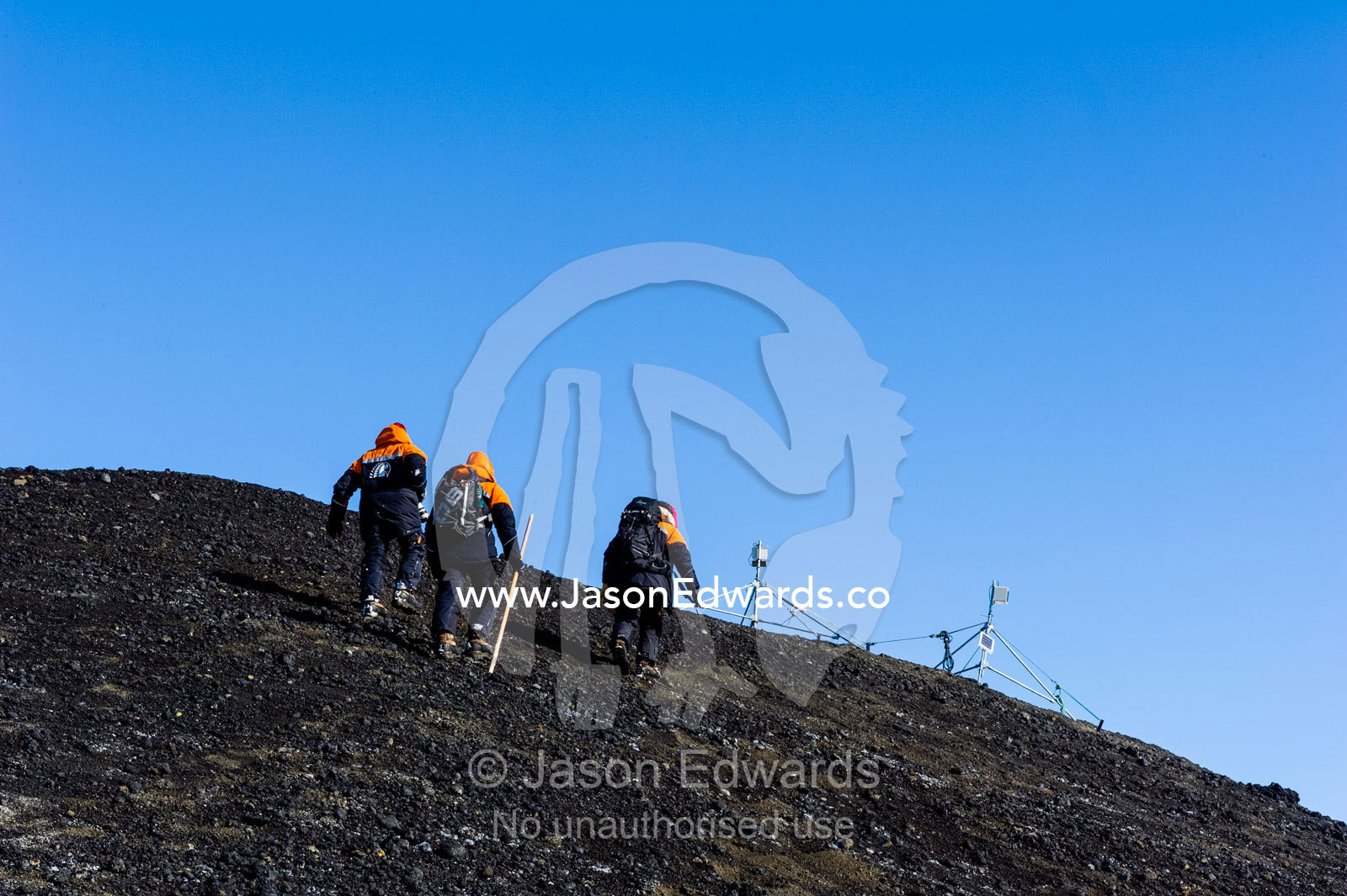 Scientists climb the slope of a volcanic island to check their camera equipment. Turtle Rock, Erebus Bay, McMurdo Sound, Ross Island, Antarctica.