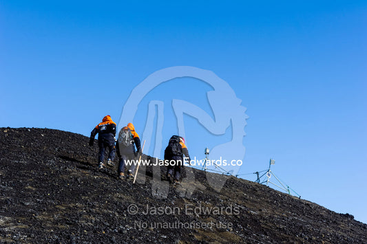 Scientists climb the slope of a volcanic island to check their camera equipment. Turtle Rock, Erebus Bay, McMurdo Sound, Ross Island, Antarctica.