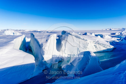 Enormous blocks of ice are pushed skyward along pressure ridges as the sea ice thins and forms melt pools. Pram Point, McMurdo Sound, Ross Island, Antarctica.