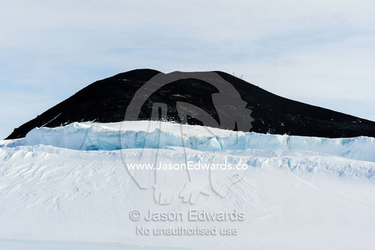 The summit of a volcanic mountain rising above pressure ridges in the sea ice. Turtle Rock, Hutton Cliffs, Erebus Bay, McMurdo Sound, Ross Island, Antarctica.