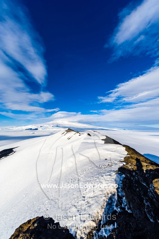 A snow-covered mountain ridge overlooking Mount Erebus an active volcano. Breached Cone, Castle Rock, Hut Point Peninsula, Ross Island, Antarctica.