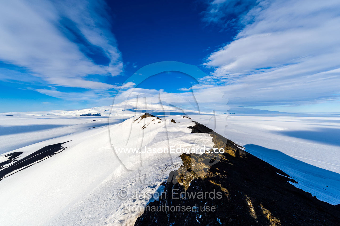 A snow-covered mountain ridge overlooking Mount Erebus an active volcano. Breached Cone, Castle Rock, Hut Point Peninsula, Ross Island, Antarctica.