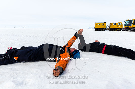 Exhausted marathon runners hold hands whilst resting on the sea ice after the race. Ross Ice Shelf, Ross Island, Antarctica.