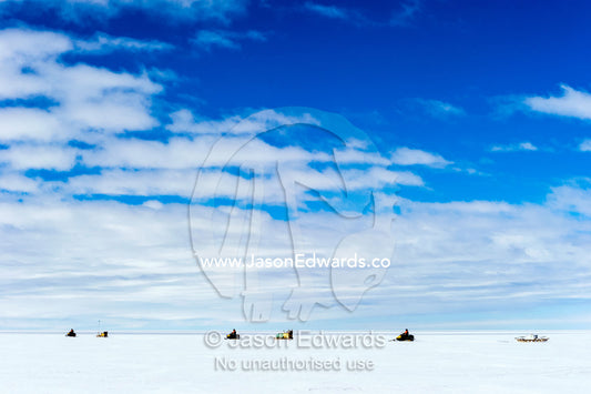 Scientists travel across the vast and featureless plain and horizon of the Ross Ice Shelf on skidoos towing a radar. Windless Bight, Ross Ice Shelf, Ross Island, Antarctica.