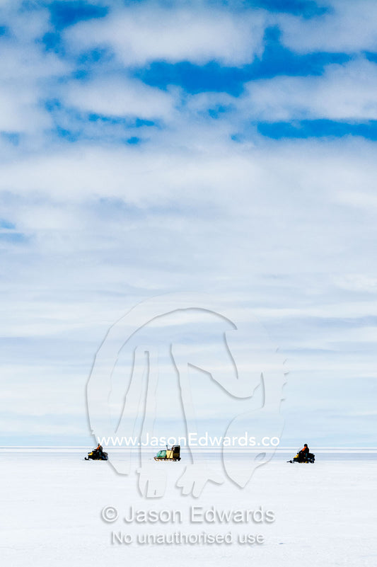 Scientists travel across the vast and featureless plain and horizon of the Ross Ice Shelf on skidoos towing a radar. Windless Bight, Ross Ice Shelf, Ross Island, Antarctica.