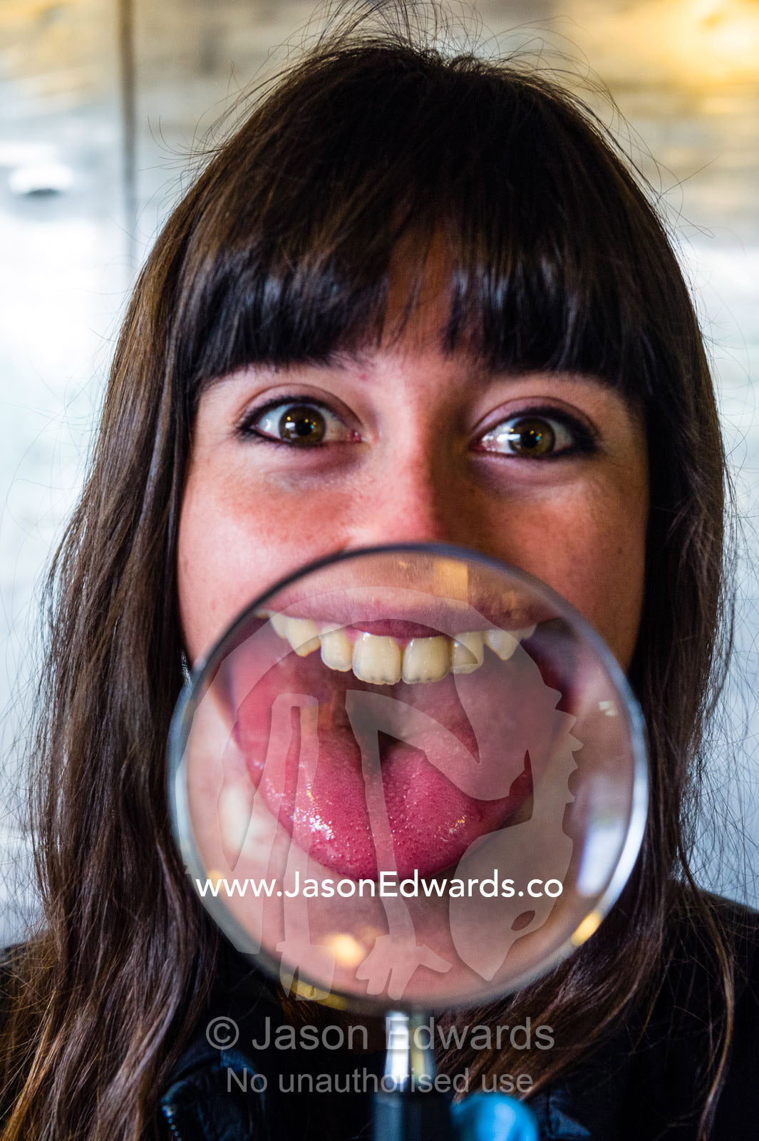 An Antarctic volunteer pokes her enlarged distorted tongue out through a magnifying glass. Scott Base, Pram Point, Hut Point Peninsula, Ross Island, Antarctica.