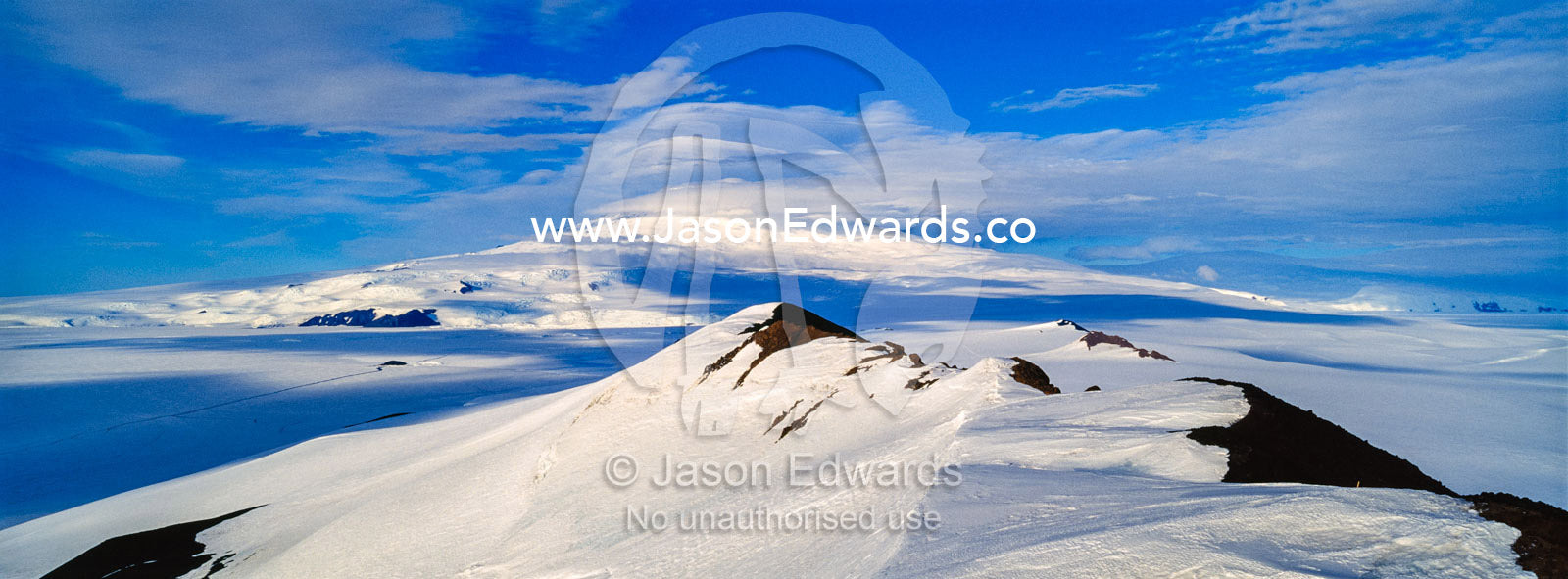A snow-covered mountain ridge overlooking Mount Erebus an active volcano. Breached Cone, Castle Rock, Hut Point Peninsula, Ross Island, Antarctica.