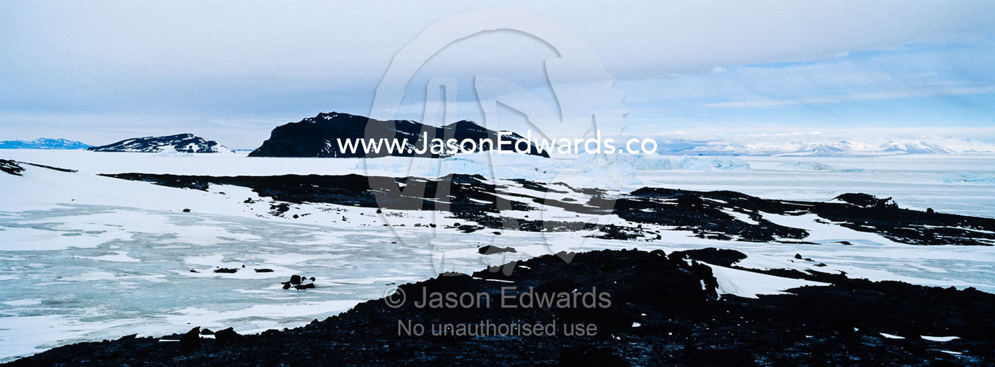 Barren and inhospitable rock encased in ice during the Antarctic summer. Cape Evans, Ross Island, Antarctica.