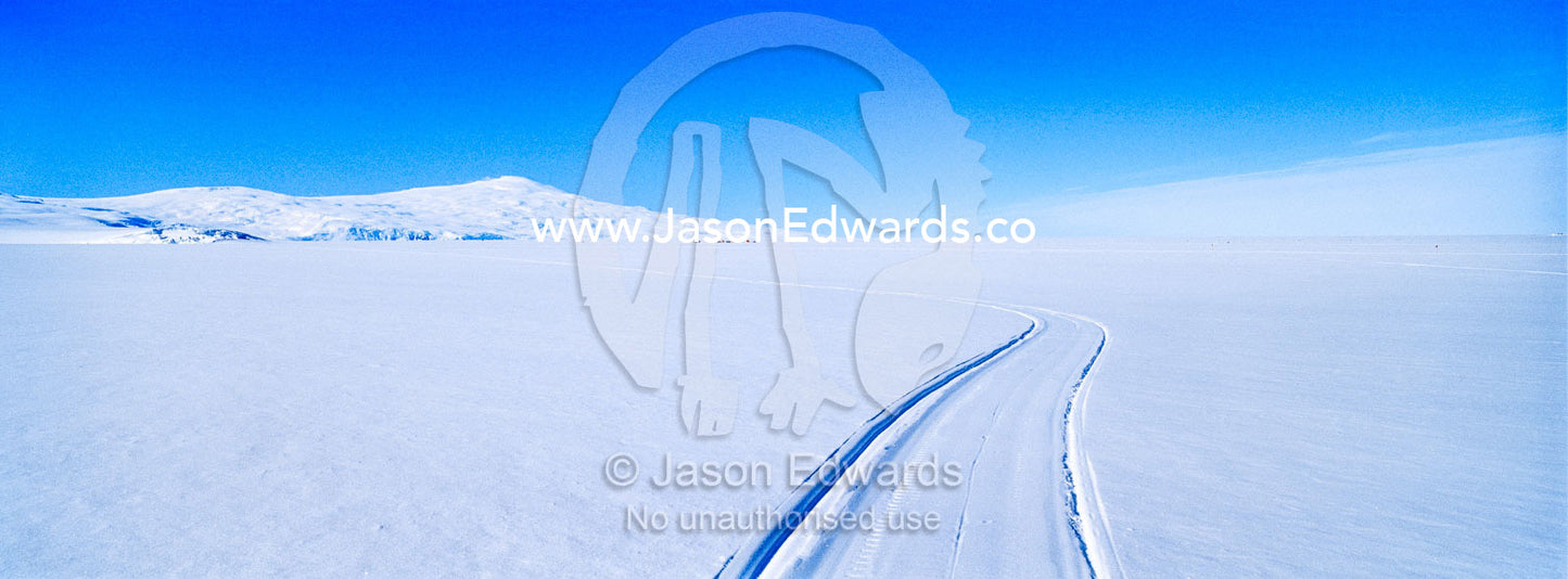 Skidoo tracks cross the Ross Ice Shelf towards Mount Erebus an active volcano. Windless Bight, Ross Ice Shelf, Ross Island, Antarctica.