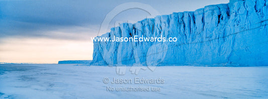 The sheer impregnable ice cliffs of a glacier tower over the frozen sea ice. Barne Glacier, Ross Sea, Ross Island, Antarctica.