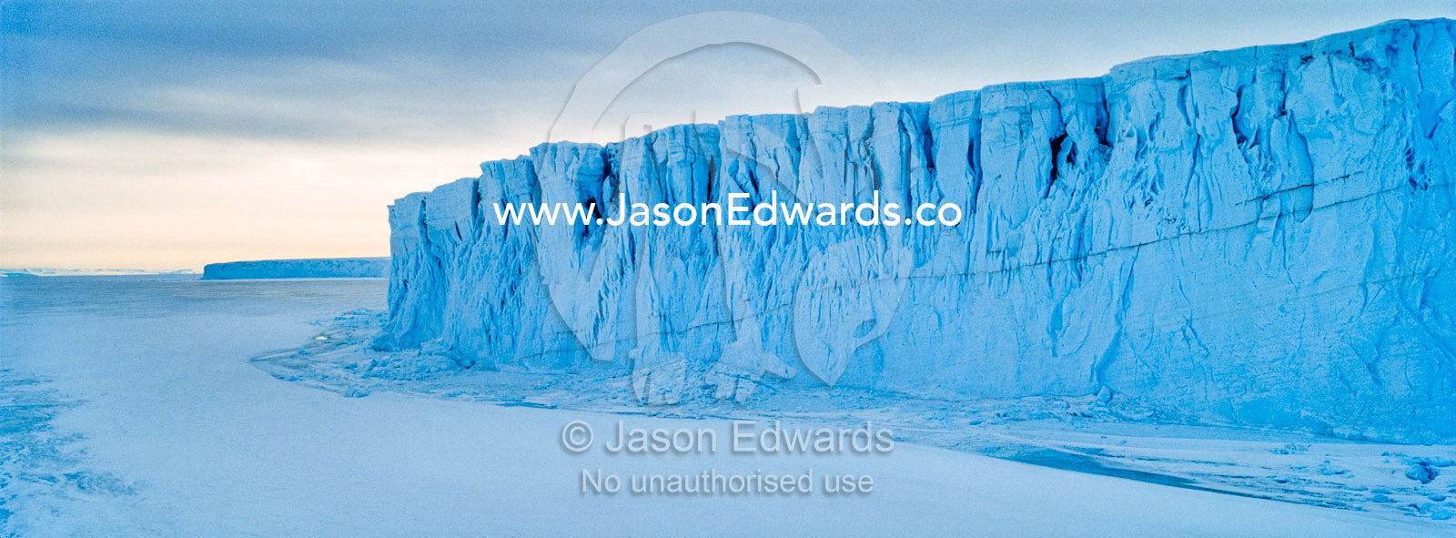 The sheer impregnable ice cliffs of a glacier tower over the frozen sea ice. Barne Glacier, Ross Sea, Ross Island, Antarctica.
