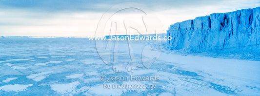 The sheer impregnable ice cliffs of a glacier tower over the frozen sea ice. Barne Glacier, Ross Sea, Ross Island, Antarctica.