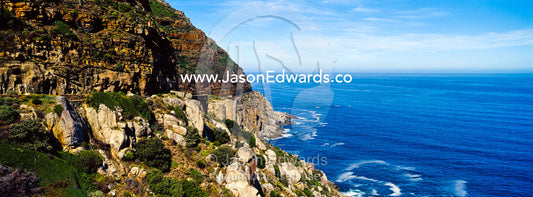 Wave foam trapped in currents along the base of coastal cliffs. Chapmans Peak Drive, Chapmans Peak Mountain Range, Cape Town, Western Cape, South Africa.