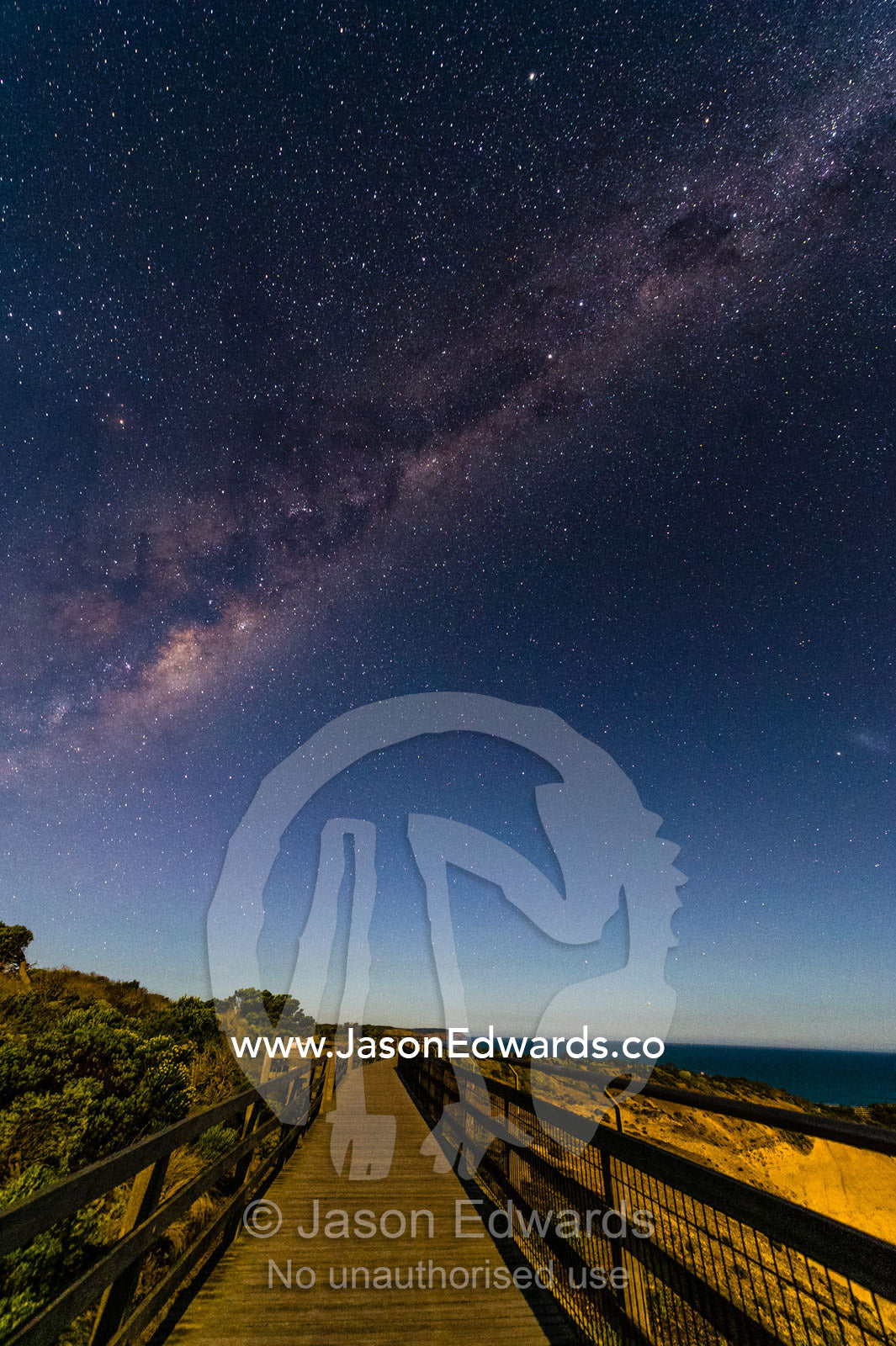 Stars in the Milky Way stretch across the night sky above a boardwalk along a coast. Twelve Apostles, Port Campbell National, Great Ocean Road, Victoria, Australia.