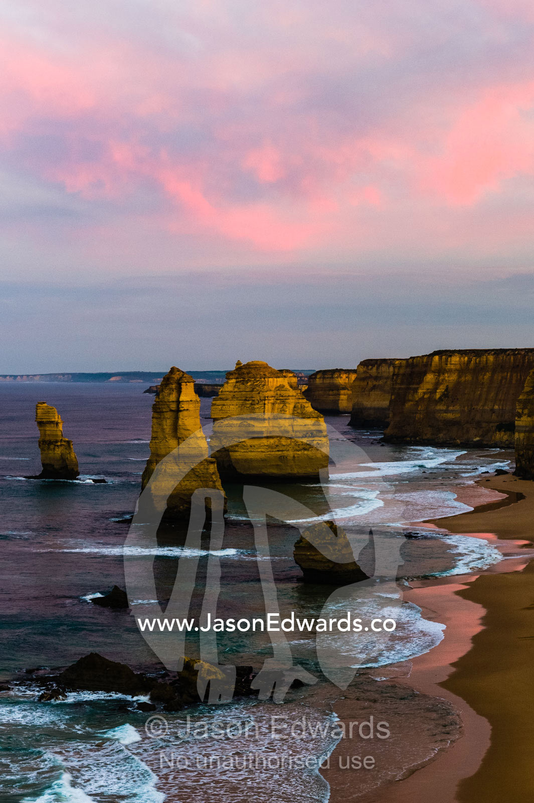 Pink pastel dawn clouds rise above the Twelve Apostles and a sheer limestone coast. Twelve Apostles, Port Campbell National, Great Ocean Road, Victoria, Australia.