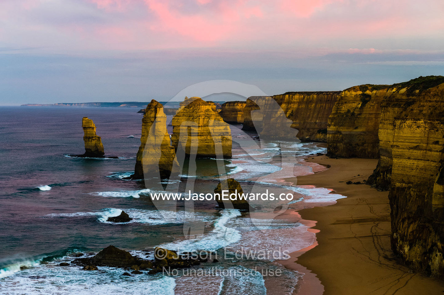 Pink pastel dawn clouds rise above the Twelve Apostles and a sheer limestone coast. Twelve Apostles, Port Campbell National, Great Ocean Road, Victoria, Australia.
