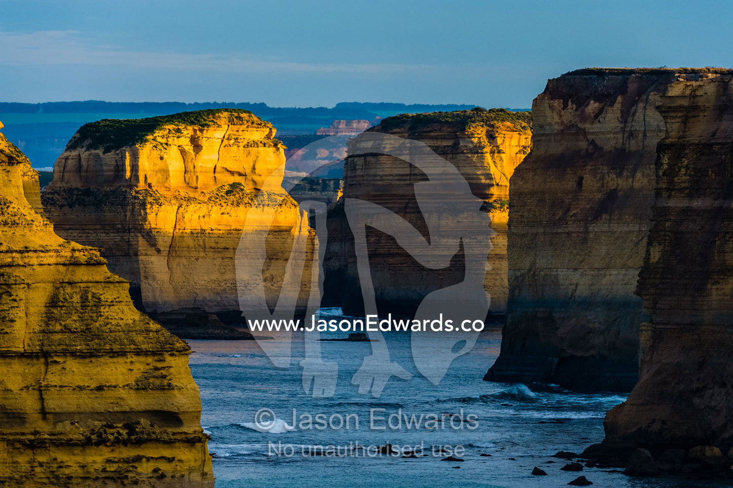 Dawn sunrays touch the sheer limestone cliffs and the Twelve Apostles pillars. Twelve Apostles, Port Campbell National, Great Ocean Road, Victoria, Australia.