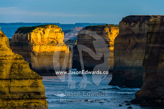 Dawn sunrays touch the sheer limestone cliffs and the Twelve Apostles pillars. Twelve Apostles, Port Campbell National, Great Ocean Road, Victoria, Australia.
