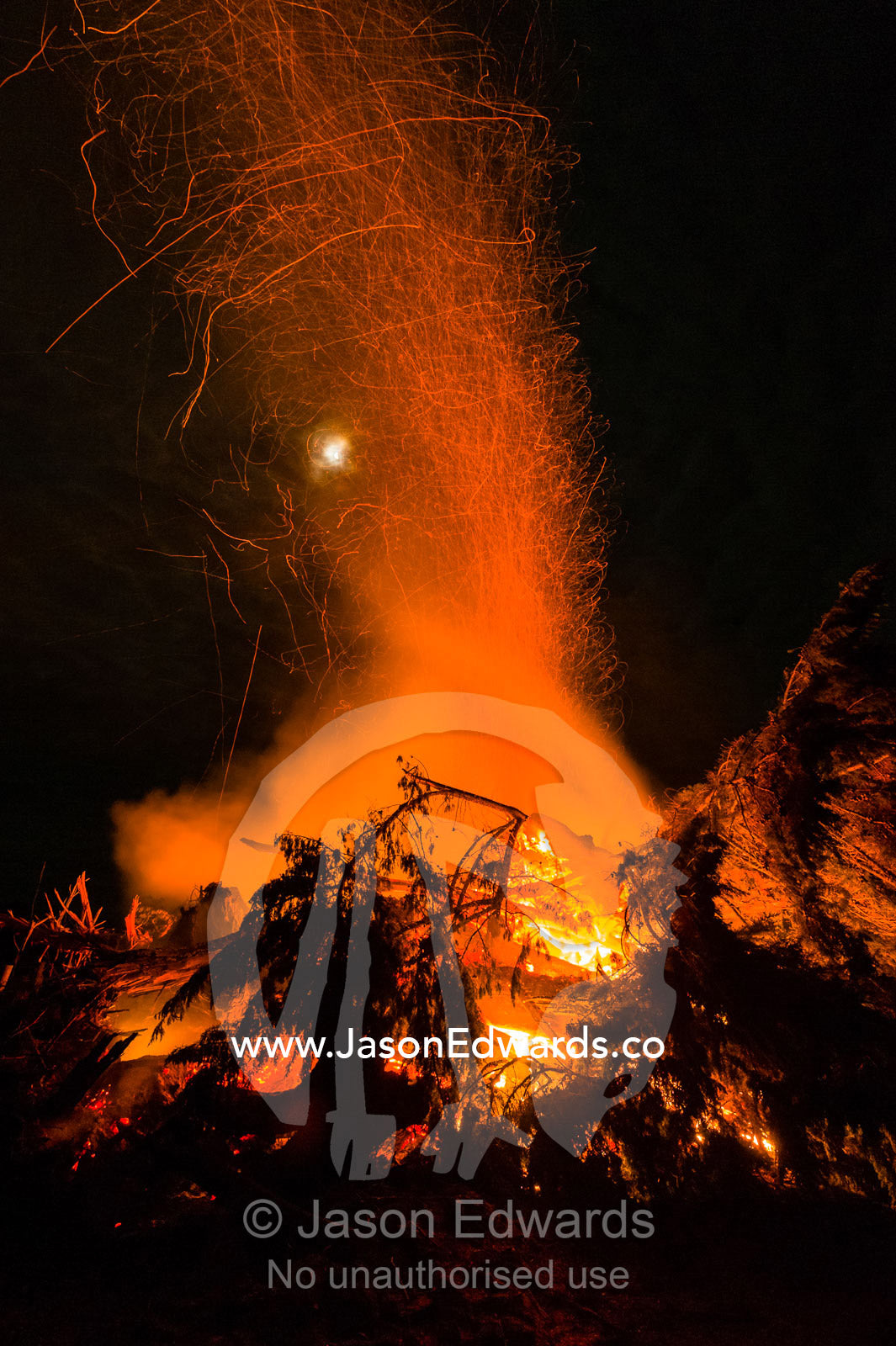 Flames and sparks fly into the air as a farmer burns surplus timber in a bonfire on his farm during winter. Bambra, Victoria, Australia.