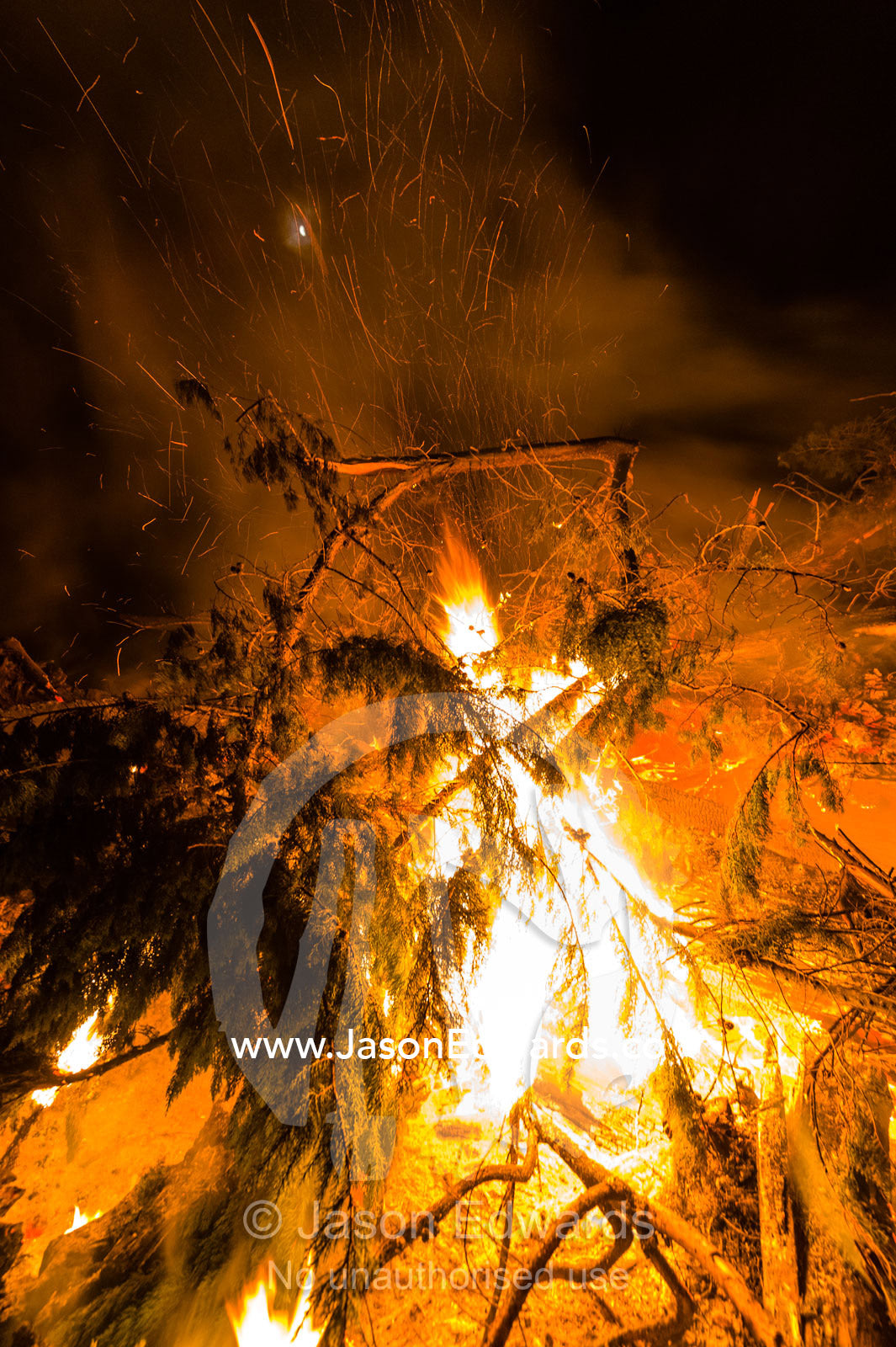 Flames and sparks fly into the air as a farmer burns surplus timber in a bonfire on his farm during winter. Bambra, Victoria, Australia.