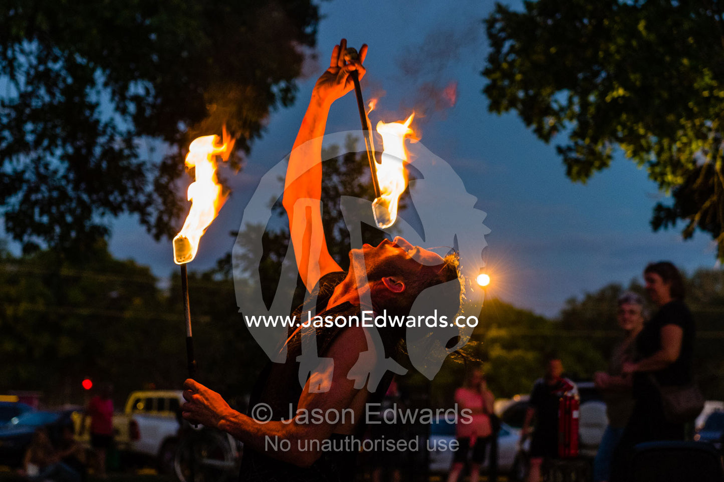 A fire performer dazzles the crowd at an open-air market by swallowing a flaming baton. Mindil Beach Sunset Markets, Darwin, Northern Territory, Australia.