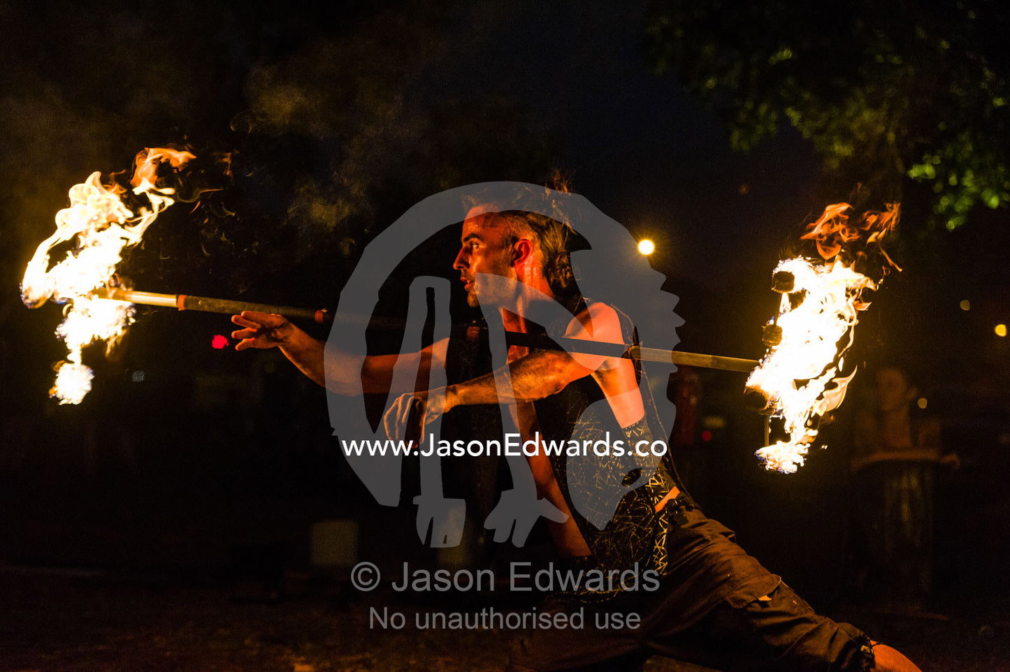 A fire performer dazzles the crowd at an open-air market by spinning a flaming baton. Mindil Beach Sunset Markets, Darwin, Northern Territory, Australia.