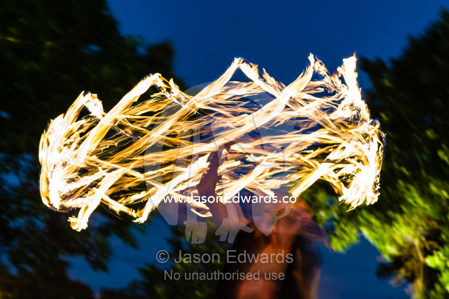 A fire performer dazzles the crowd at an open-air market by spinning and twirling a flaming baton. Mindil Beach Sunset Markets, Darwin, Northern Territory, Australia.
