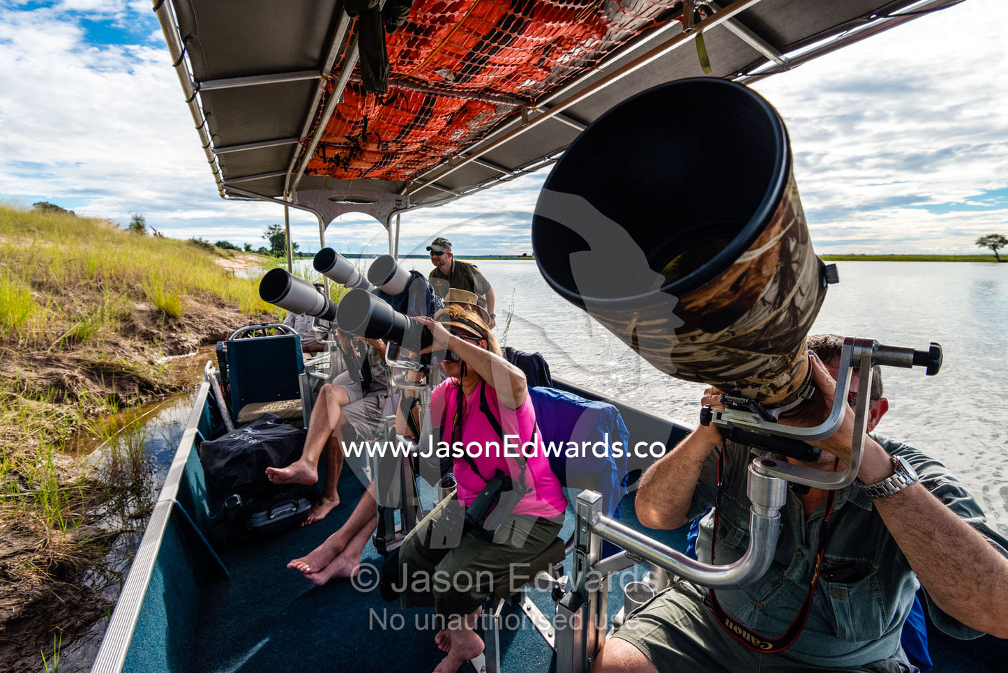 A group of tourists photographing wildlife from a boat on a river. Chobe River, Chobe National Park, Botswana.
