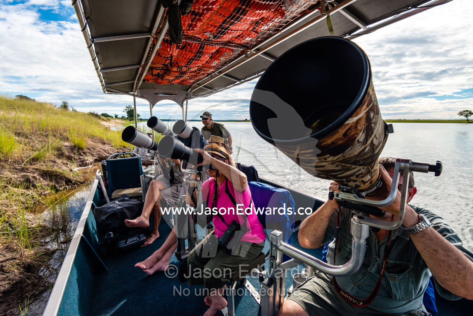 A group of tourists photographing wildlife from a boat on a river. Chobe River, Chobe National Park, Botswana.
