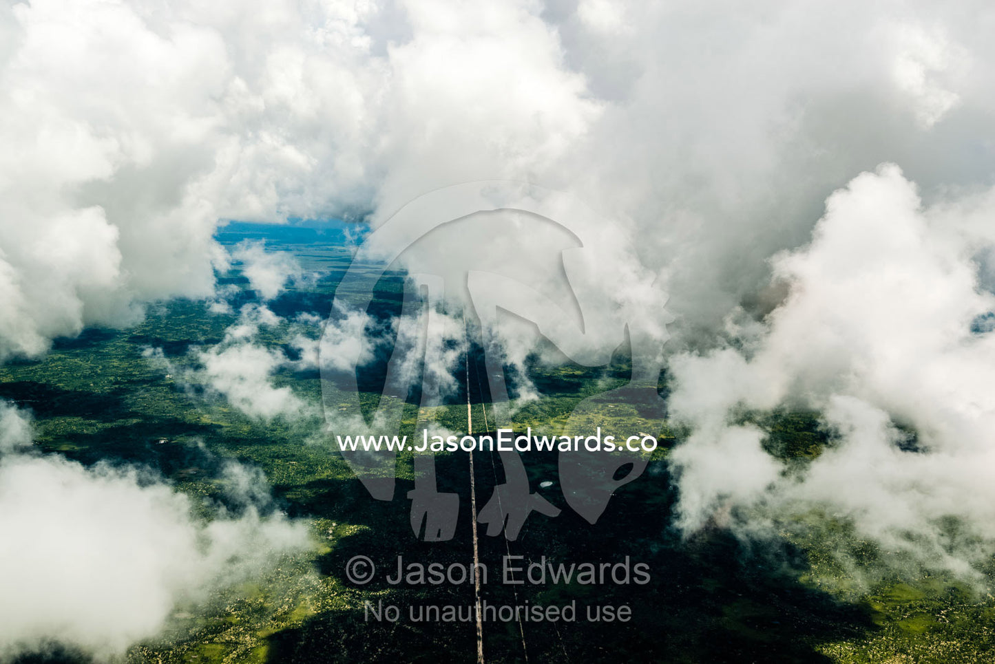 An aerial view of a long straight road running through the African wilderness beneath storm clouds. Chobe National Park, Botswana.