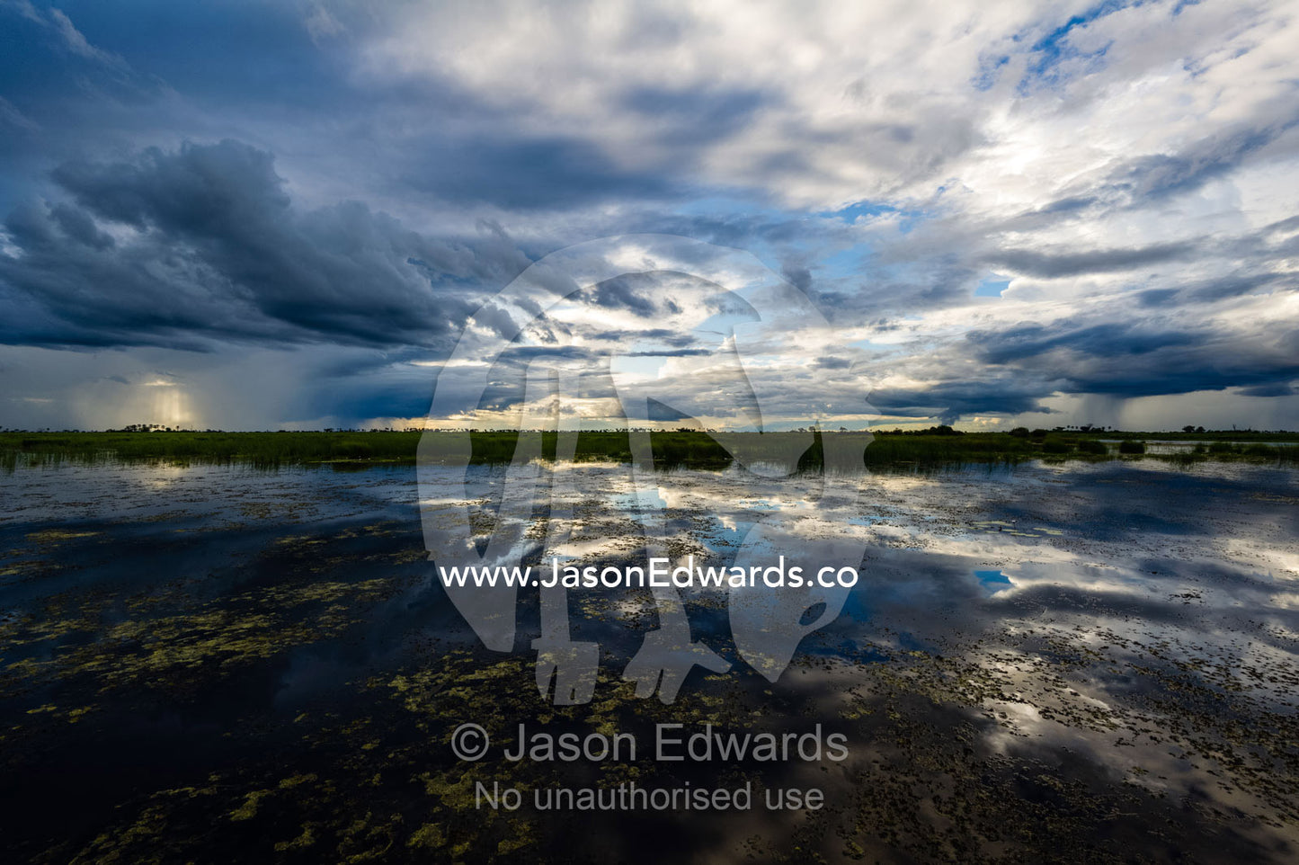 The reflection of storm clouds at sunset across the still surface of a wetland. Zarafa Camp, Zibadianja Lagoon, Savute Channel, Linyanti, Botswana.