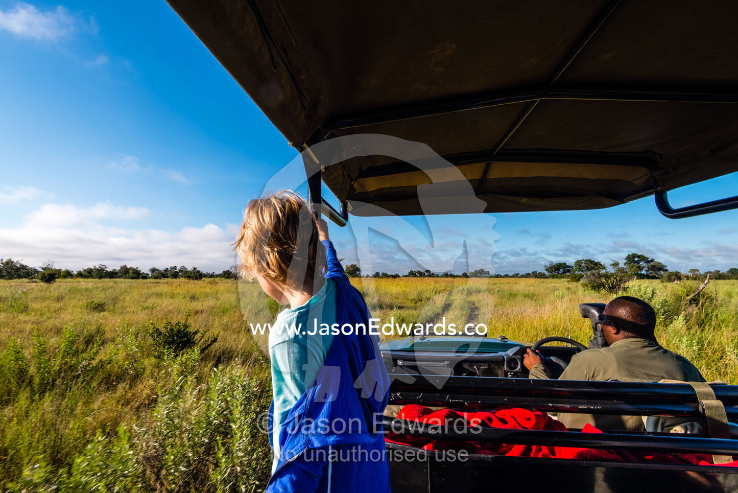 A small boy searches for wildlife from a safari 4wd on a floodplain. Selinda Reserve, Linyanti Region, Northern Botswana.