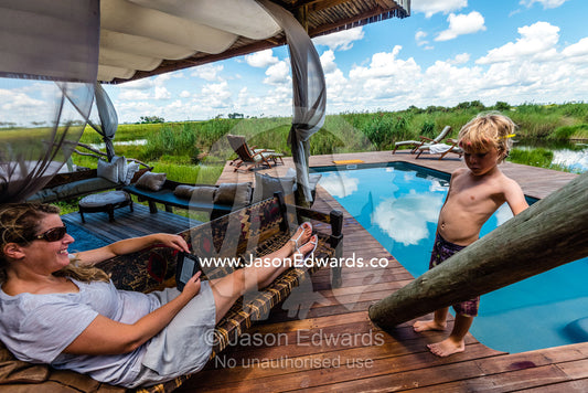A boy and his mother relaxing by the pool of a luxury safari camp. Selinda Camp, Selinda Reserve, Linyanti Region, Northern Botswana.